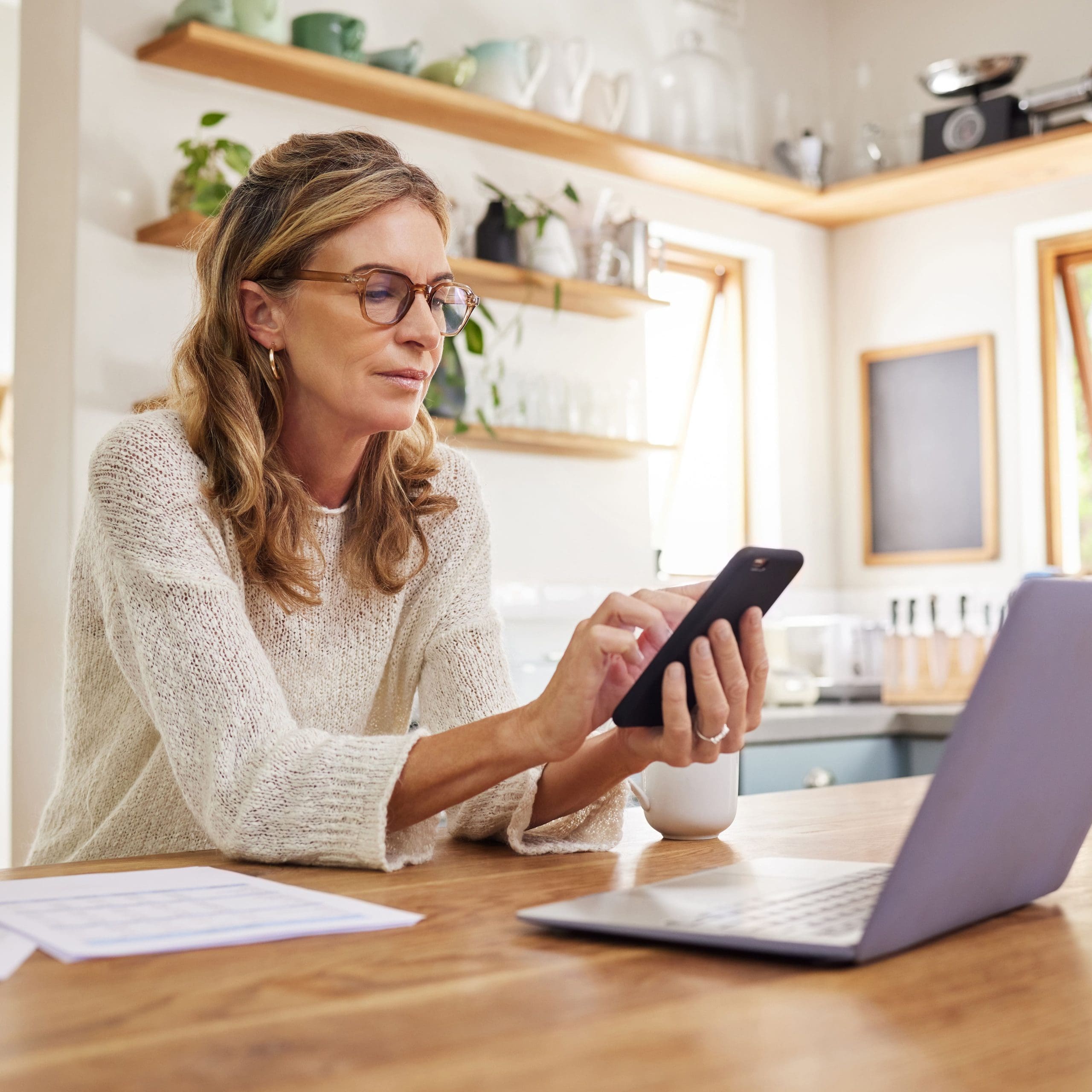 Woman, laptop or fintech phone app in house or home kitchen for finance budget, investment accounting or insurance taxes. Thinking mature person with technology, paper or document for retirement loan.